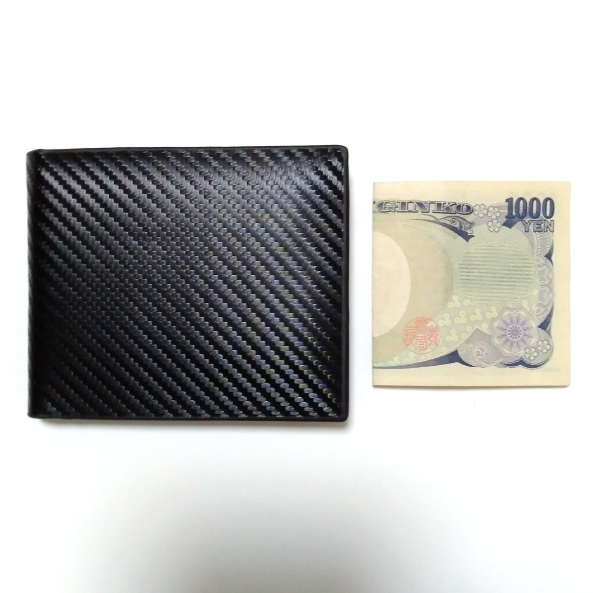2つ折り財布 カラー：ブラック カーボン調 スリム 小さい コンパクト 黒 お札入れ カード入れ 小銭入れ ビジネス おしゃれ メンズ 合皮_大きさの比較に千円札を置いています